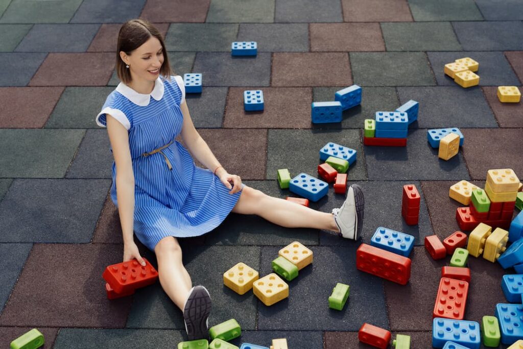 Femme assise sur des dalles en caoutchouc pour terrasse avec des blocs colorés, un espace sûr et confortable pour les enfants.