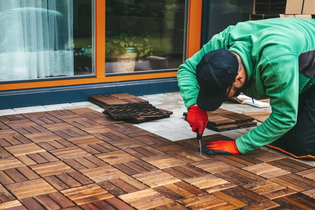 Ouvrier installant un different revetement de sol exterieur en dalles de bois sur une terrasse extérieure, avec outils et gants de protection pour une pose impeccable