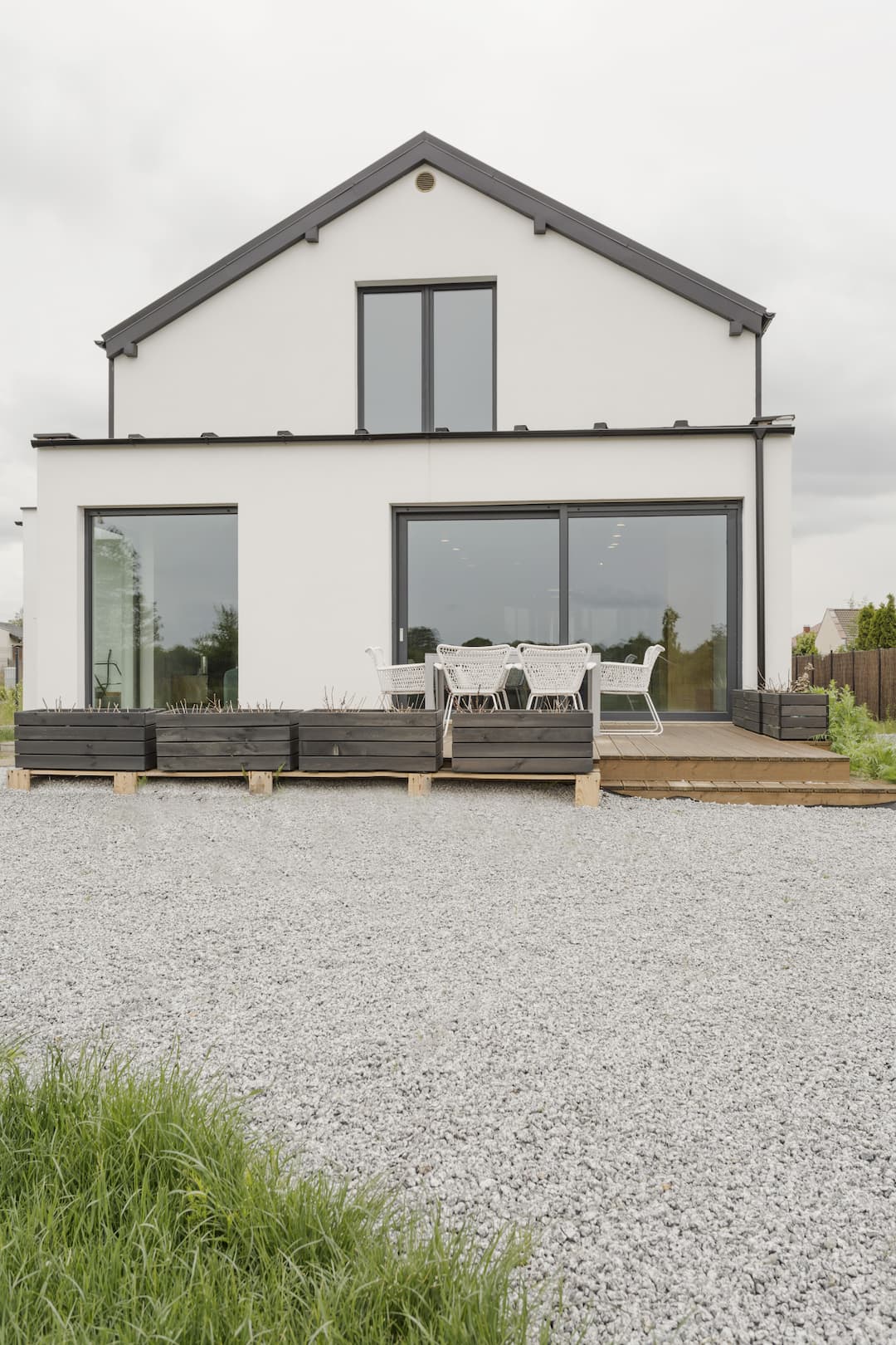 Maison moderne blanche avec terrasse en bois, mobilier extérieur et gravier. Idéal pour une terrasse sur sable ou des aménagements paysagers.