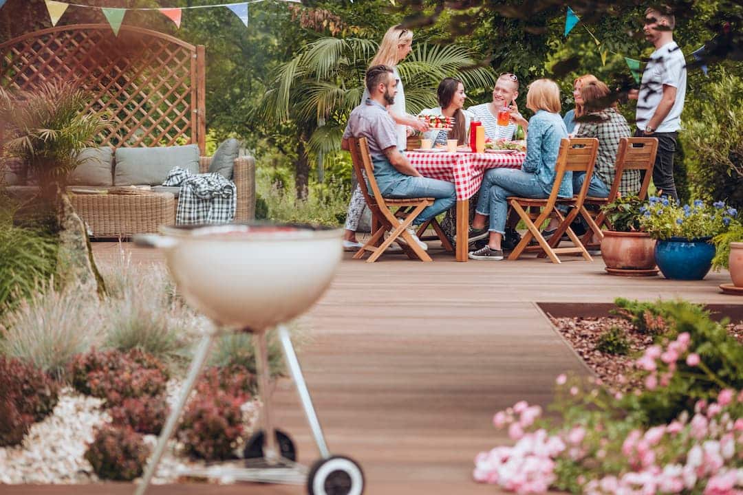 Des amis profitent d'un barbecue et d'un repas convivial sur une terrasse pas chère en bois, décorée de guirlandes, dans un jardin.
