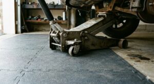 Cric de voiture reposant sur des dalles PVC grises, mettant en &eacute;vidence la caract&eacute;ristique technique des dalles PVC pour la r&eacute;sistance et la protection du sol de garage.